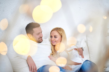 A beautiful happy young couple sitting on the sofa in the living room with christmas lights.