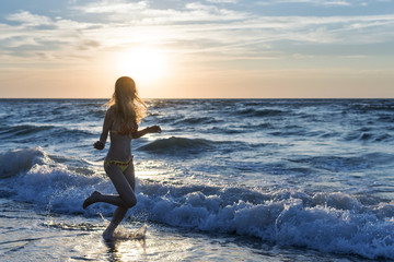 Woman runs along the surf line near the sea at dawn