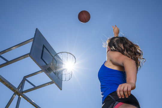 Young woman playing basketball, against the sun
