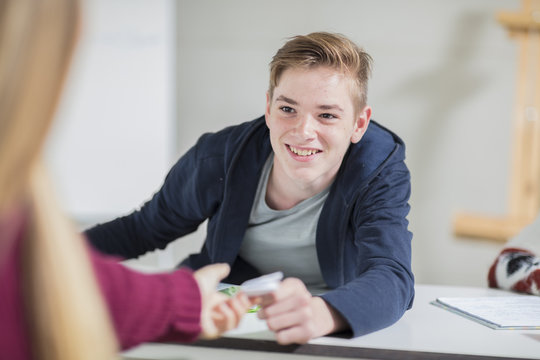 Smiling teenage boy passing a note to a girl in class