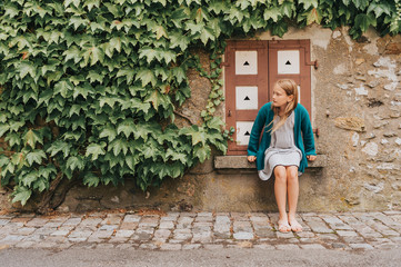 Outdoor fashion portrait of a cute little girl against ivy wall