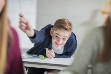 Smiling teenage boy passing a note in class