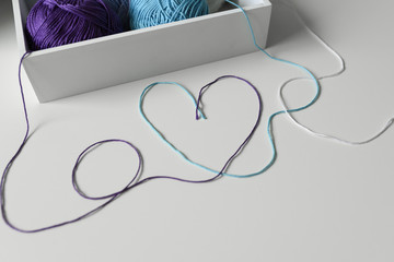 Love word and heart designed from colorful wool threads on white table from knitting yarn in a wood box.
