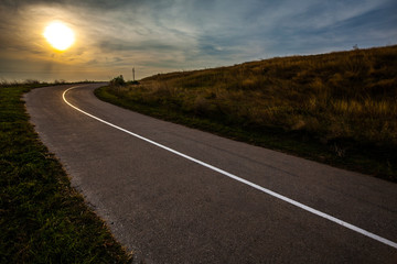 blue sky over empty asphalt road during Sunset. Field of golden grass