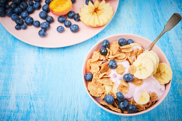 Healthy breakfast bowl berry greek yoghurt with frefh blueberries, banana and flakes on the blue wooden table