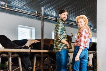 happy couple of farmers looking at camera in stable with cows