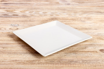 Perspective view. white square plate on a wooden table