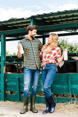 couple of farmers holding bottles of cow milk near stable and looking at each other