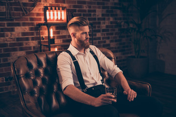 Portrait of stunning serious confident handsome thinking pondering pensive focused concentrated relaxed dreamy planning entrepreneur sitting on leather divan enjoying alcohol beverage in hands