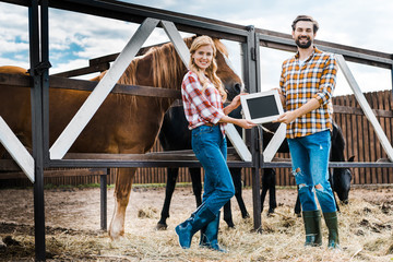 smiling couple of farmers holding blackboard in stable