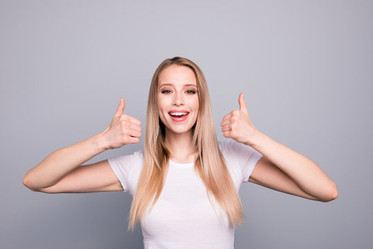 Portrait of young caucasian, charming, attractive gorgeous cute smiling girl wearing casual white t-shirt showing thumbs up. Isolated over grey background