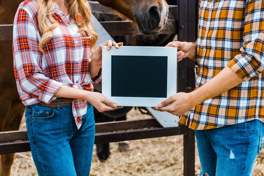 cropped image of couple of farmers holding blackboard in stable