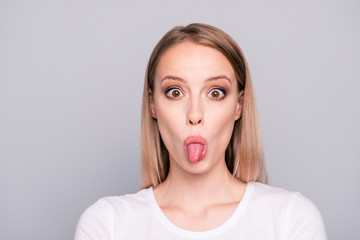 Portrait of young lovely girl wearing white t-shirt showing tongue out. Isolated over grey background, copy space