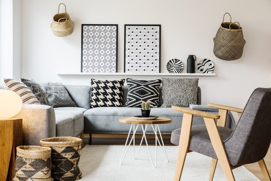 Grey wooden armchair in scandi living room interior with patterned posters above settee. Real photo