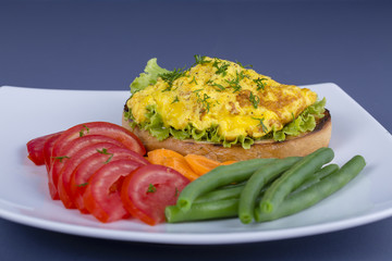 Egg omelette on a piece of fried bread with green beans, red tomato and carrot on a plate, close up. Breakfast concept