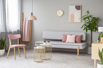 Real photo of lounge with dirty pink pillows, simple poster, pink chair, gold end tables with...