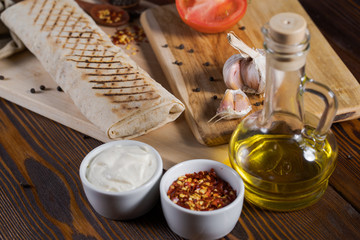Shawarma chicken roll in a pita with fresh vegetables and cream sauce on wooden background.