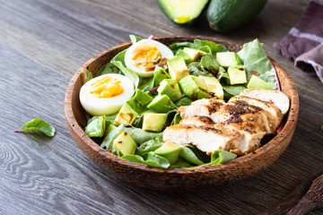 Green lunch bowl with grilled chicken, avocado and eggs. Healthy and dietary food. Space for text.