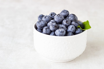 Fresh blueberries in a white vintage ceramic bowl with mint on light grey background. Copy space