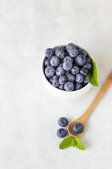 Fresh blueberries in a white vintage ceramic bowl and wooden spoon with mint on light grey background. Copy space
