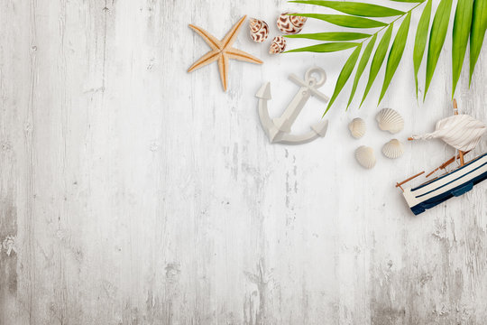 Palm leaves, seashells, boat, starfish anchor and other decoration on white wooden desk with empty space. Flat lay