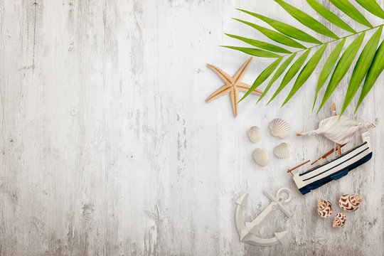Palm leaves, seashells, boat, starfish anchor and other decoration on white wooden desk. Flat lay