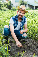 happy handsome farmer planting pumpkin seeds in field at farm