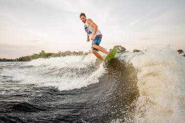 Naklejka premium Active wakesurfer jumping on board riding down the river waves