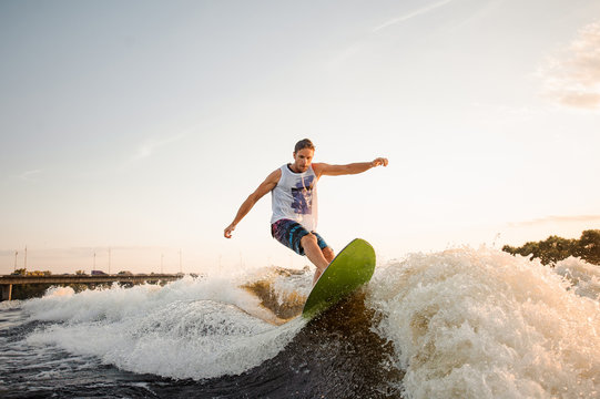 Active man riding on green wakesurf down the river waves