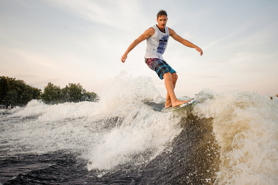 Active and strong wakesurfer riding down the river on board