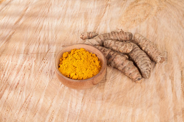Turmeric powder and fresh turmeric on wooden background