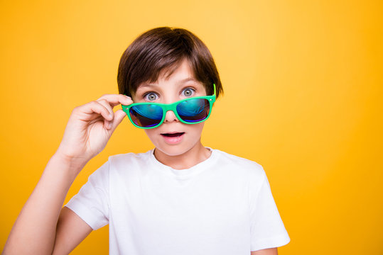 Portrait of attractive young cheerful amazed surprised school boy, smiling putting glasses down over yellow background, isolated. Copyspace