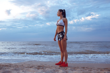 the girl does a warm-up before doing sports early in the morning on the seashore. A girl of athletic build with a dry muscle mass