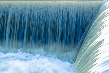 Small dam with motion of water flowing rapids. Seen as lines and patterns with foam.