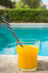 Glass of Freshly Pressed Tropical Fruits Orange Juice with Striped Straw on Deck of Villa Swimming Pool on Sunny Summer Day. Vacation Relaxation Travel Luxury. Authentic Atmosphere