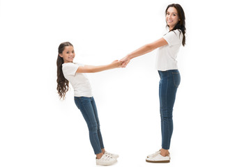 side view of happy mother and daughter in white shirts holding hands isolated on white