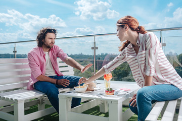 Obraz premium Lifting hand. Red-haired woman lifting her hand for trying fries of boyfriend while having lunch on summer terrace together