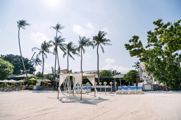 Wedding venue with minimal flower decoration on the beach, white cover chairs with blue stripes...