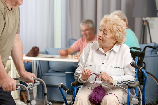 Senior woman in wheelchair knitting while talking with her friend at care home