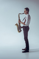 side view of stylish young professional musician playing saxophone on grey