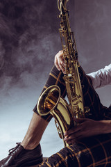 Obraz na płótnie Canvas cropped shot of stylish musician holding saxophone in smoke on grey