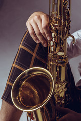 close-up partial view of stylish professional musician holding saxophone on grey