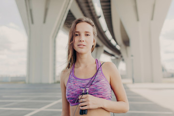 Obraz premium Healthy beautiful female European female uses jumping rope, dressed in casual top, has fitness training outdoor alone, motivates young people to go in for sport and keep fit. Athletic woman.