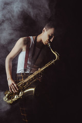 handsome young musician playing saxophone in smoke on black