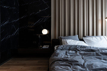 Cozy bedroom corner with nice black marble table lamp in mid century style in front of  wooden strip composition  headboard and natural black marble on the wall