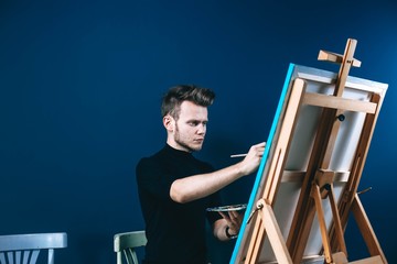 beautiful male artist paints a painting in the studio on canvas. blue background for your text.
