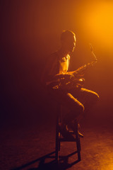 Naklejka premium young stylish jazzman sitting on stool and holding saxophone