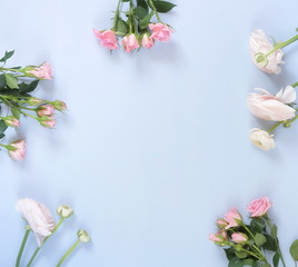 Fototapeta premium Flowers background. Bouquet frame of pale pink ranunculus and roses flowers on pale blue background. Top view. Copy