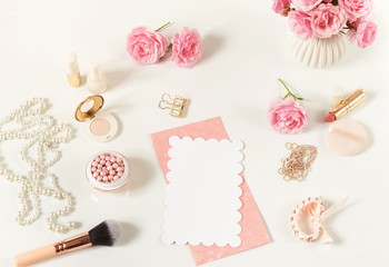Makeup cosmetic accessories products pearl make up powder and brush, lipstick, perfume, pale pink roses flowers and blank for text on white background. Flat lay. Top view. Copy space