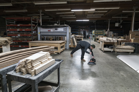 An employee sweeping up after work hours in a large woodworking factory.